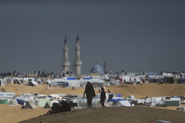 فلسطينيون نزحوا بسبب الهجوم البري الإسرائيلي على قطاع غزة يسيرون في مخيم الخيام المؤقت في رفح، قطاع غزة، الأحد، 18 فبراير، 2024. (AP Photo/Mohammed Dahman)