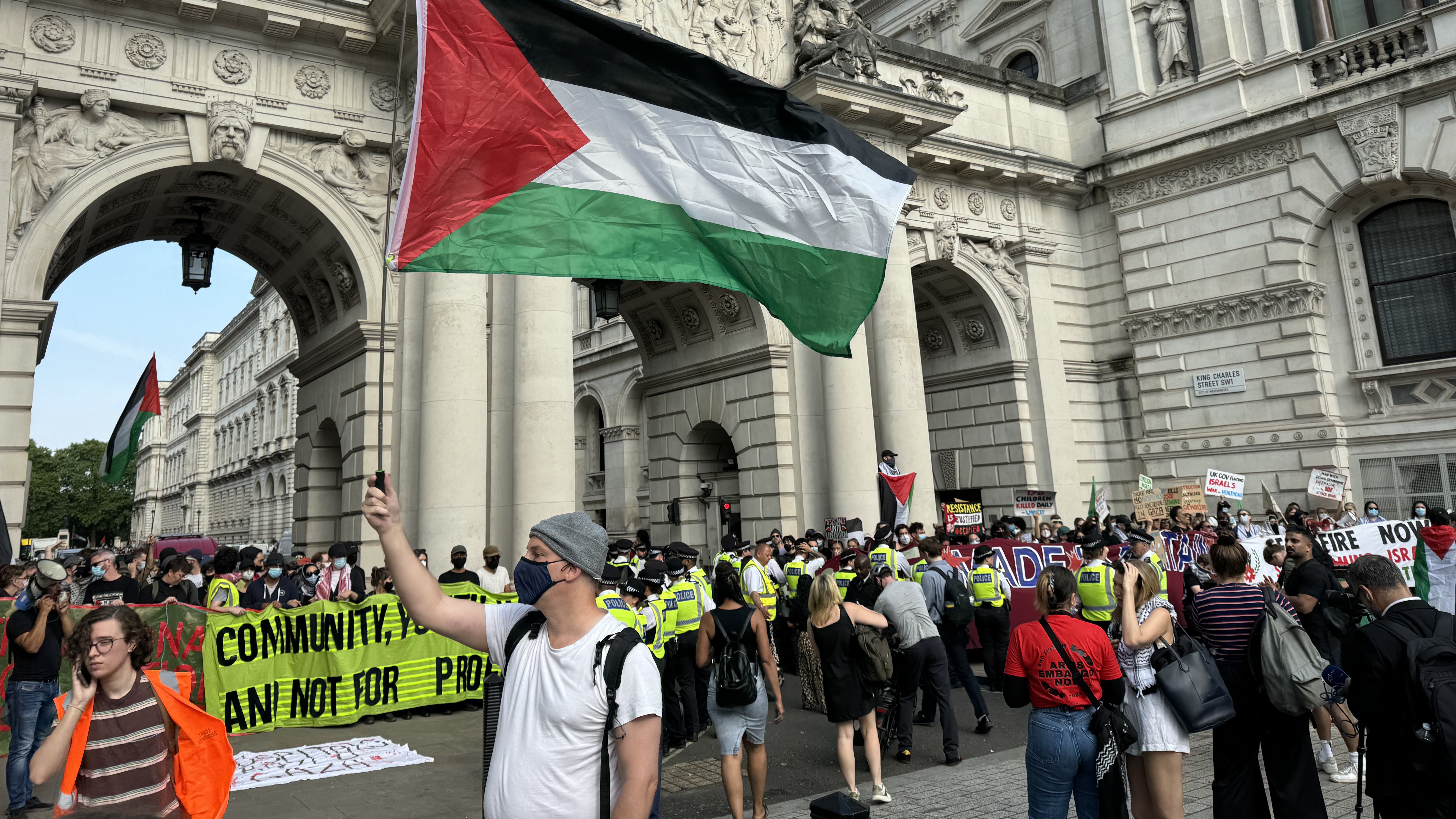رجل يرفع العلم الفلسطيني أمام مدخل وزارة الخارجية المحاصر في لندن يوم الأربعاء (محمد صالح/ميدل إيست آي)