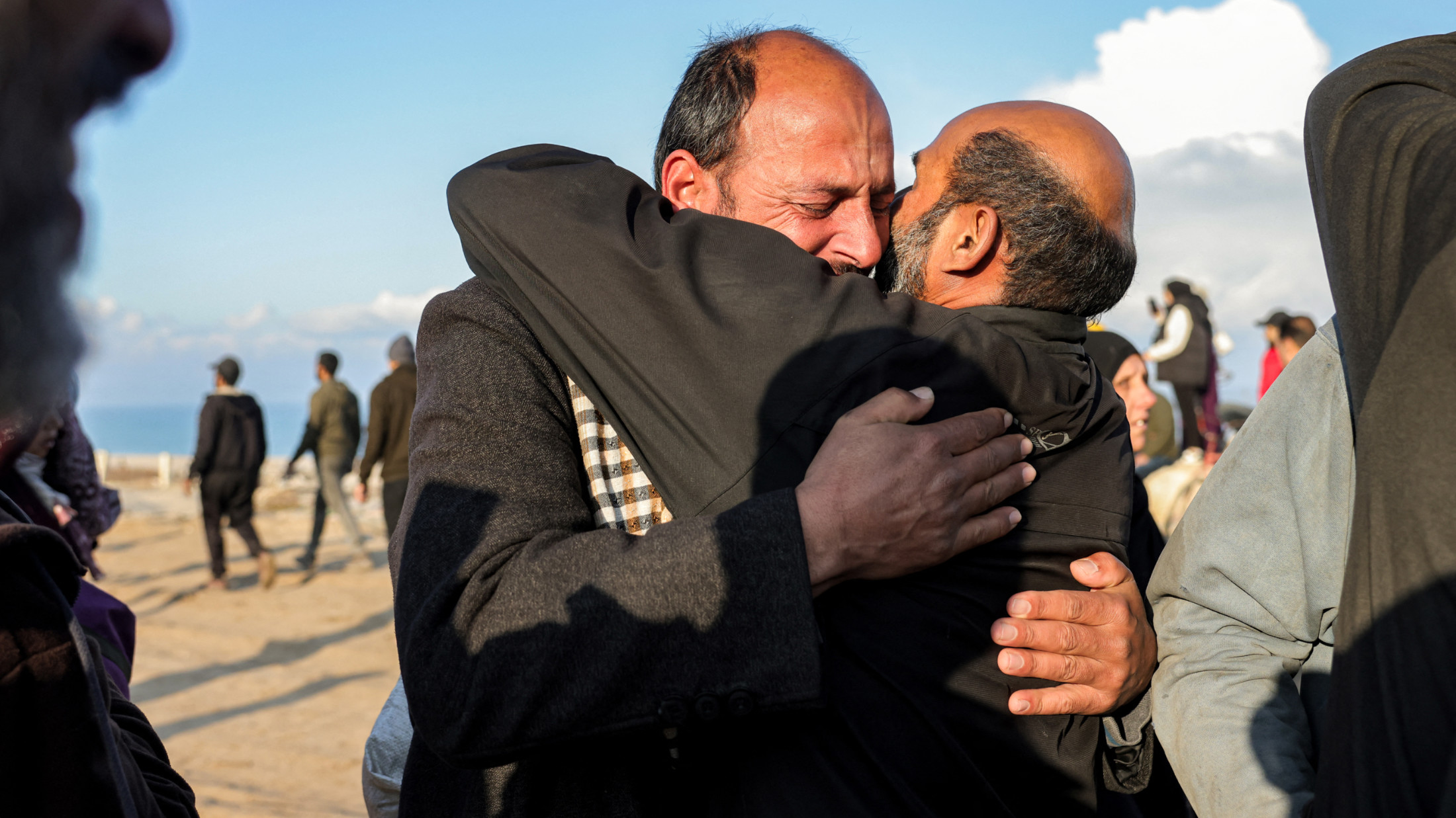 رجل يحتضن آخر بعد أن عبر ممر Netzarim من قطاع غزة الجنوبي شمالًا إلى مدينة غزة على طول شارع الرشيد الساحلي في غزة في 27 يناير 2025 (AFP/Bashar Taleb)