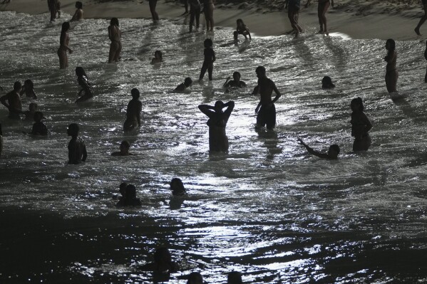 الناس يخوضون في مياه Arpoador Beach بينما تغرب الشمس في ريو دي جانيرو ، 23 يناير 2025. (AP Photo/Silvia Izquierdo ، ملف)