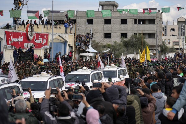 يتجمع الفلسطينيون بينما يرافق مقاتلو حماس مركبات الصليب الأحمر قبل تسليم الرهائن الإسرائيليين في نوسائر ، قطاع غزة وسط يوم السبت ، 22 فبراير 2025. (AP Photo/Abdel Kareem Hana)