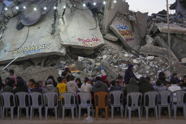 يجلس الفلسطينيون على طاولة كبيرة محاطًا بركوب المنازل والمباني المدمرة أثناء تجمعهم من أجل الإفطار ، وجبة سريعة ، في اليوم الأول من رمضان في رافح ، جنوب غزة ، السبت ، 1 مارس 2025 (AP Photo/Abdel Kareem Hana)