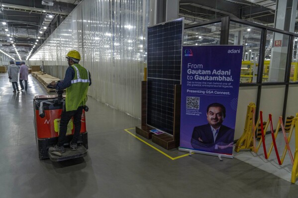 عجلات مشغل حمولة رافعة تتجاوز شاشة لوحة شمسية إلى جانب صورة لـ Gautam Adani داخل Mundra Solar Techno-Park Private Limited ، في مدينة موندرا ميندرا في ولاية غوجارات في غوجارات ، الهند ، في 20 سبتمبر ، 2023 (AP Photo/Rafiq Maqbool ، ملف)