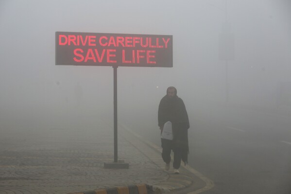 رجل يسير عبر لافتة تقرأ "Drive Save Life" في Peshawar ، باكستان ، 23 يناير 2024. (AP Photo/Muhammad Sajjad ، ملف)