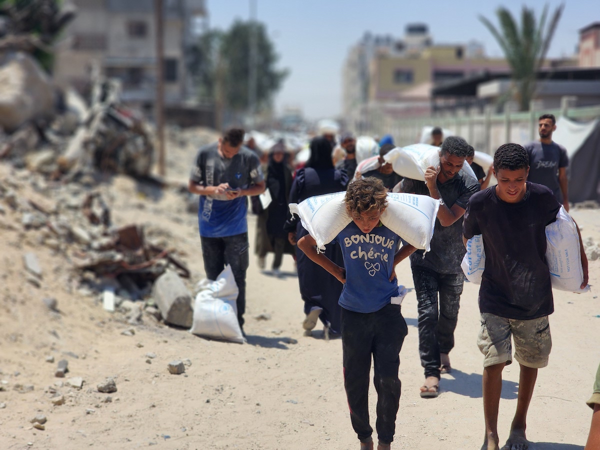 يحمل الفلسطينيون ، الذين يكافحون مع الجوع وسط هجمات إسرائيلية مستمرة ، أكياس الدقيق التي تلقوها في نقطة توزيع المساعدات التي وزعها برنامج الأغذية العالمي (WFP) في خان يونيس ، غزة في 23 يوليو 2025.