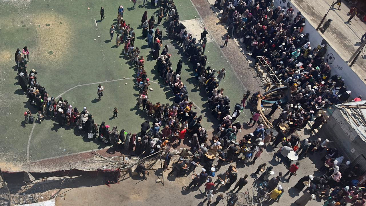 شوهد الفلسطينيون في غزة يصطفون لساعات في الشمس الحارقة ، يائسة من أجل مغرفة واحدة من الطعام ، في صورة تم التقاطها من قبل صديق المؤلف آية ناصر من نافذة غرفة نومها في يوليو 2025 (تم توفيرها)