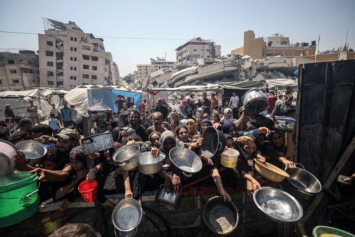 الفلسطينيون الذين يحملون المقالي ، يجتمعون لتلقي وجبات ساخنة ، وزعت من قبل منظمة خيرية في مدينة غزة ، حيث يكافح السكان للوصول إلى الطعام بسبب الحصار الإسرائيلي المستمر والهجمات في مدينة غزة ، غزة في 23 يوليو 2025.