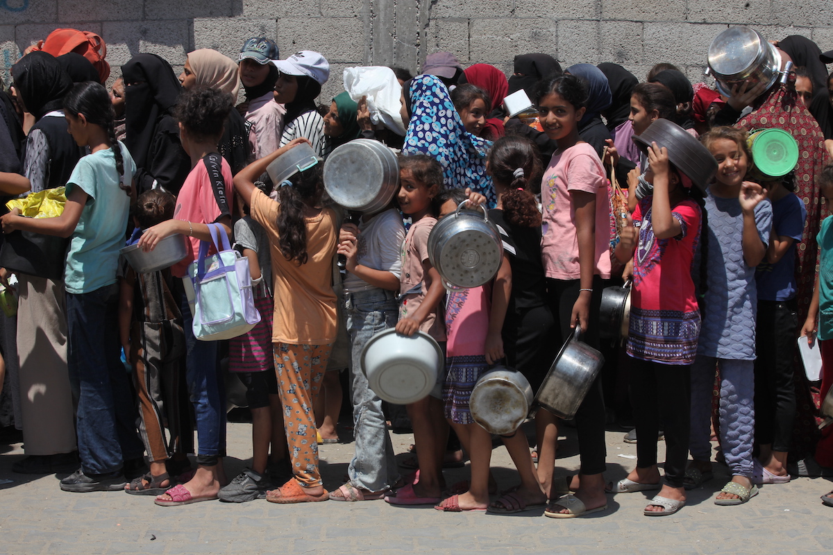 فلسطينيون ، بمن فيهم الأطفال ، الذين يكافحون للوصول إلى الطعام بسبب الحصار الإسرائيلي والهجمات المستمرة على قطاع غزة ، ينتظرون في طابور لتلقي وجبات ساخنة وزعتها المنظمة الخيرية في معسكر نوسيرات للاجئين في دير بالة ، غزة في 18 أغسطس ، 2025.