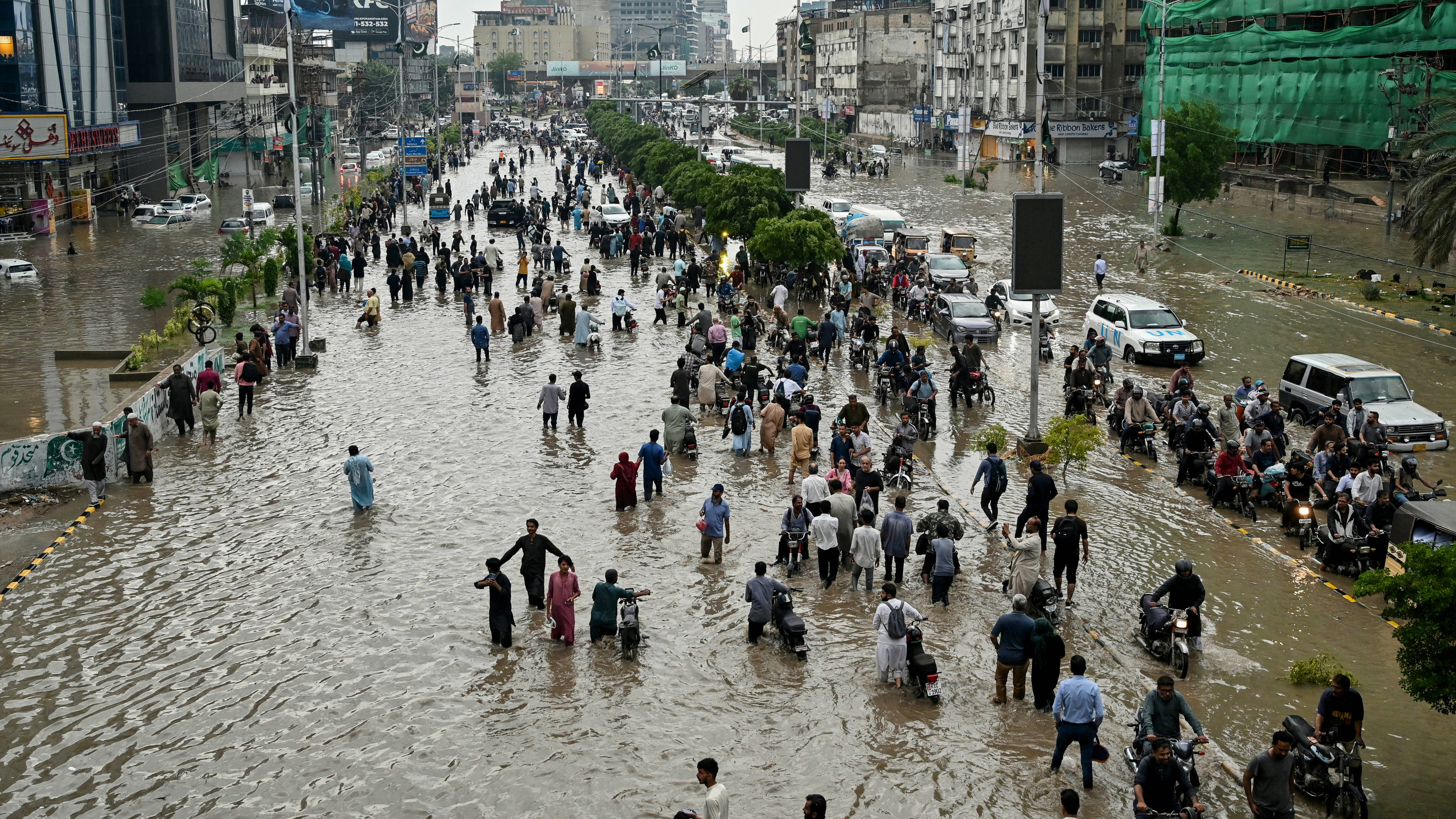 الناس يتجولون في شارع غمرته المياه بعد هطول الأمطار الغزيرة في كراتشي في 19 أغسطس (Asif Hassan / AFP)