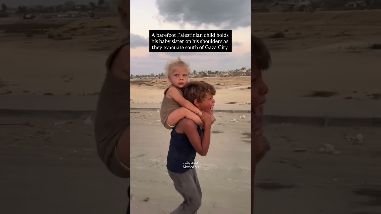 طفل فلسطيني حافي القدمين يحمل شقيقه على كتفيه أثناء إجلاءهم جنوب مدينة غزة (ScreenGrab/Ahmed Younis)
