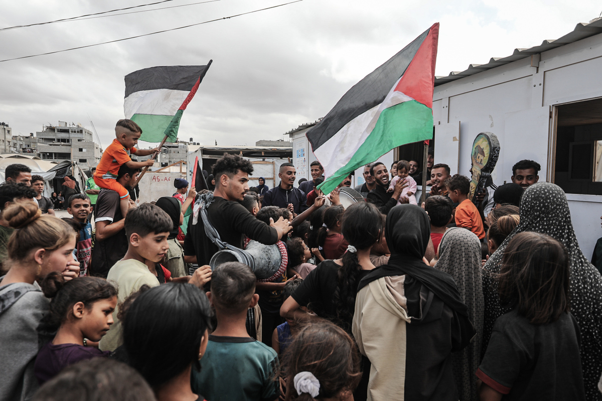 فلسطينيون، بينهم أطفال، متجمعون في مخيم النصيرات للاجئين يحتفلون بالأعلام الفلسطينية بعد إعلان اتفاق وقف إطلاق النار في غزة في 09 أكتوبر 2025 في دير البلح، غزة. (معز صالحي – وكالة الأناضول)