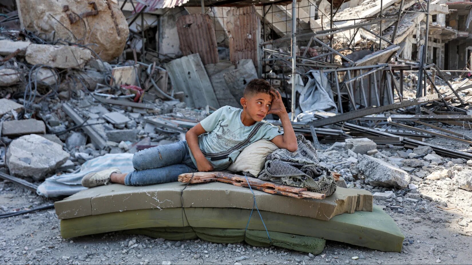 طفل فلسطيني يستريح بالقرب من الأنقاض بعد انسحاب القوات الإسرائيلية من خان يونس، جنوب قطاع غزة، 10 أكتوبر 2025 (Omar al-Qattaa/AFP)